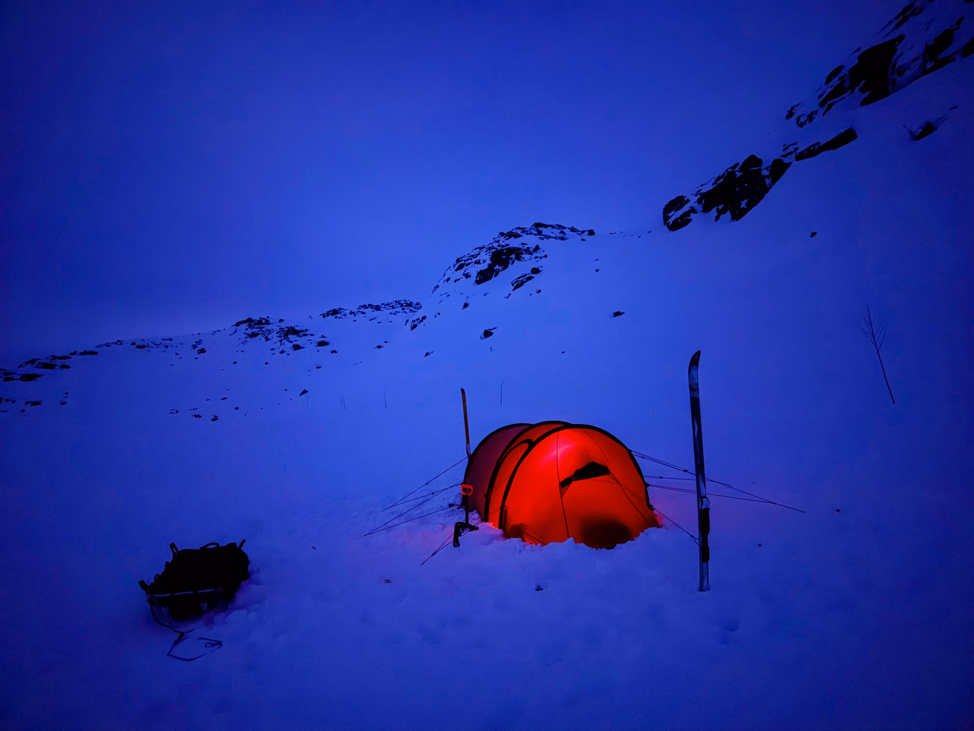 A red tent in the snow with a blue sky above.