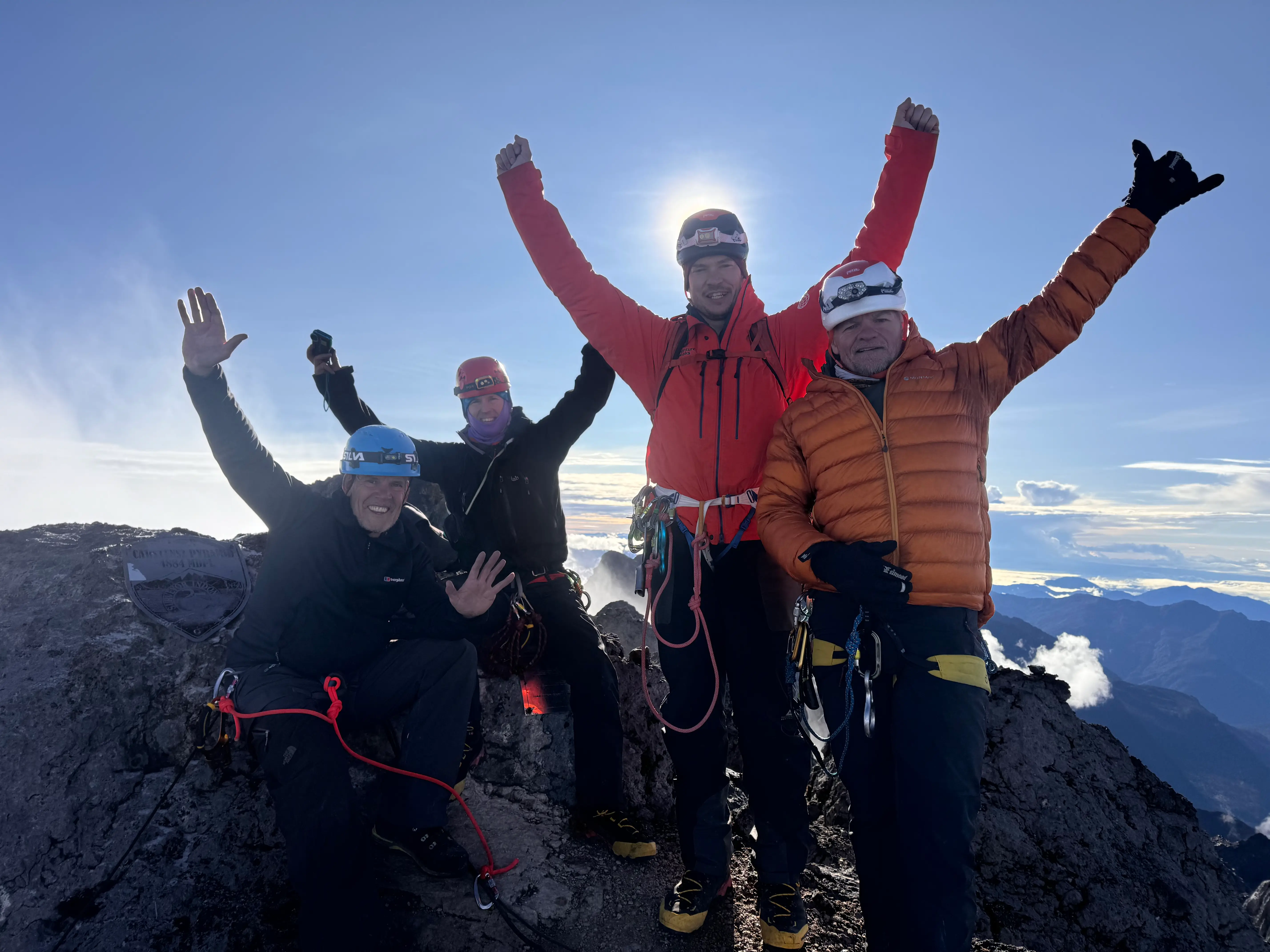 Four climbers in helmets and down jackets raising their arms on the summit of Carstensz Pyramid