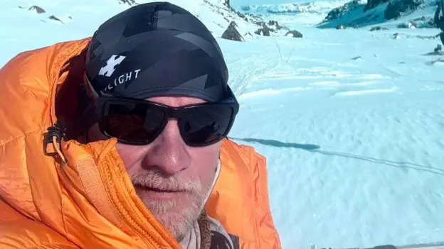 A climber in an orange down jacket, hat and sunglasses on a snow covered slope