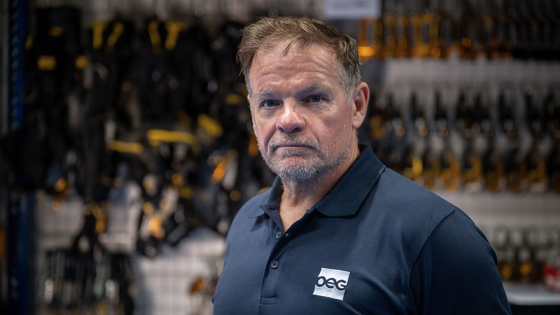 A man in a navy polo shirt with an OEG logo standing in front of racks of hanging equipment