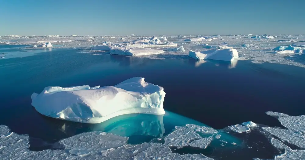 Icebergs and broken sea ice drifting in dark blue Arctic water under a clear pale sky