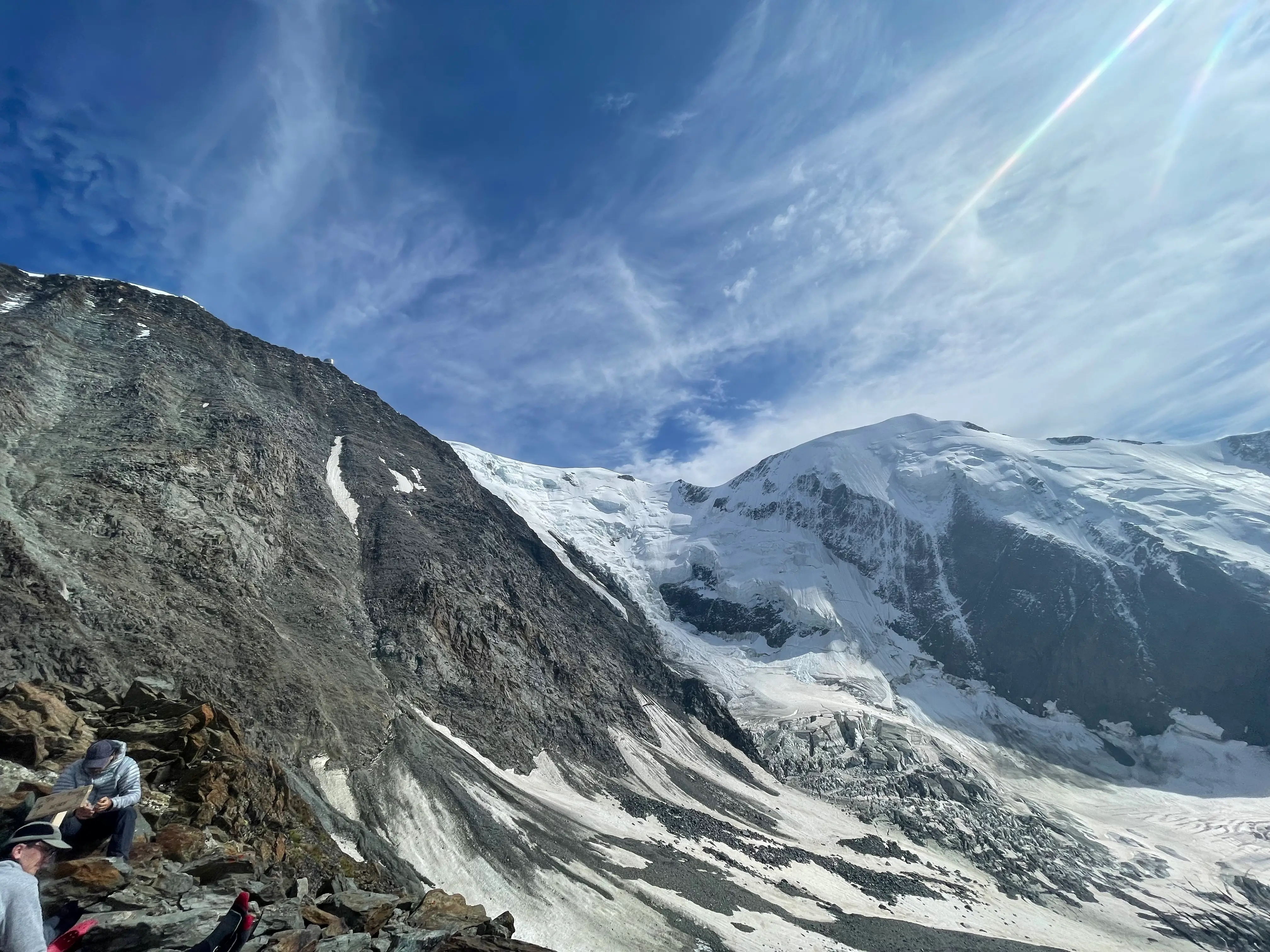 Climbers resting on a rocky ridge below the glaciated slopes of Mont Blanc under a blue sky