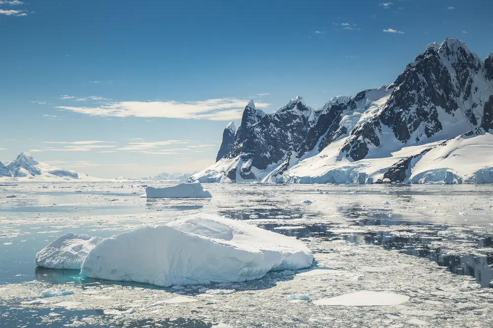 Icebergs drifting in ice strewn Antarctic waters below dark, snow covered peaks