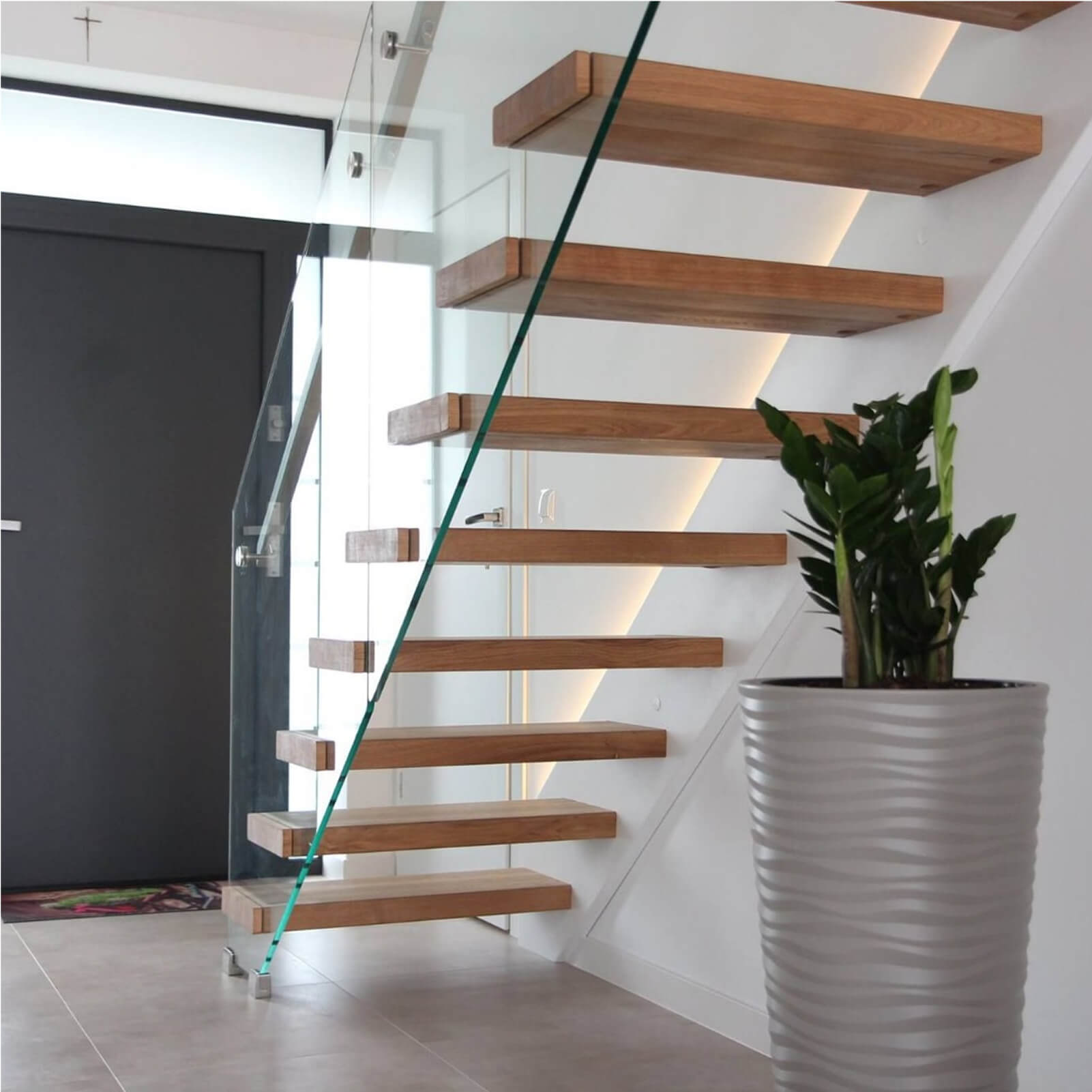 Ekskluzywne schody metalowo-drewniane z otwartymi stopniami i balustradą ze szkła hartowanego oraz roślina w donicy