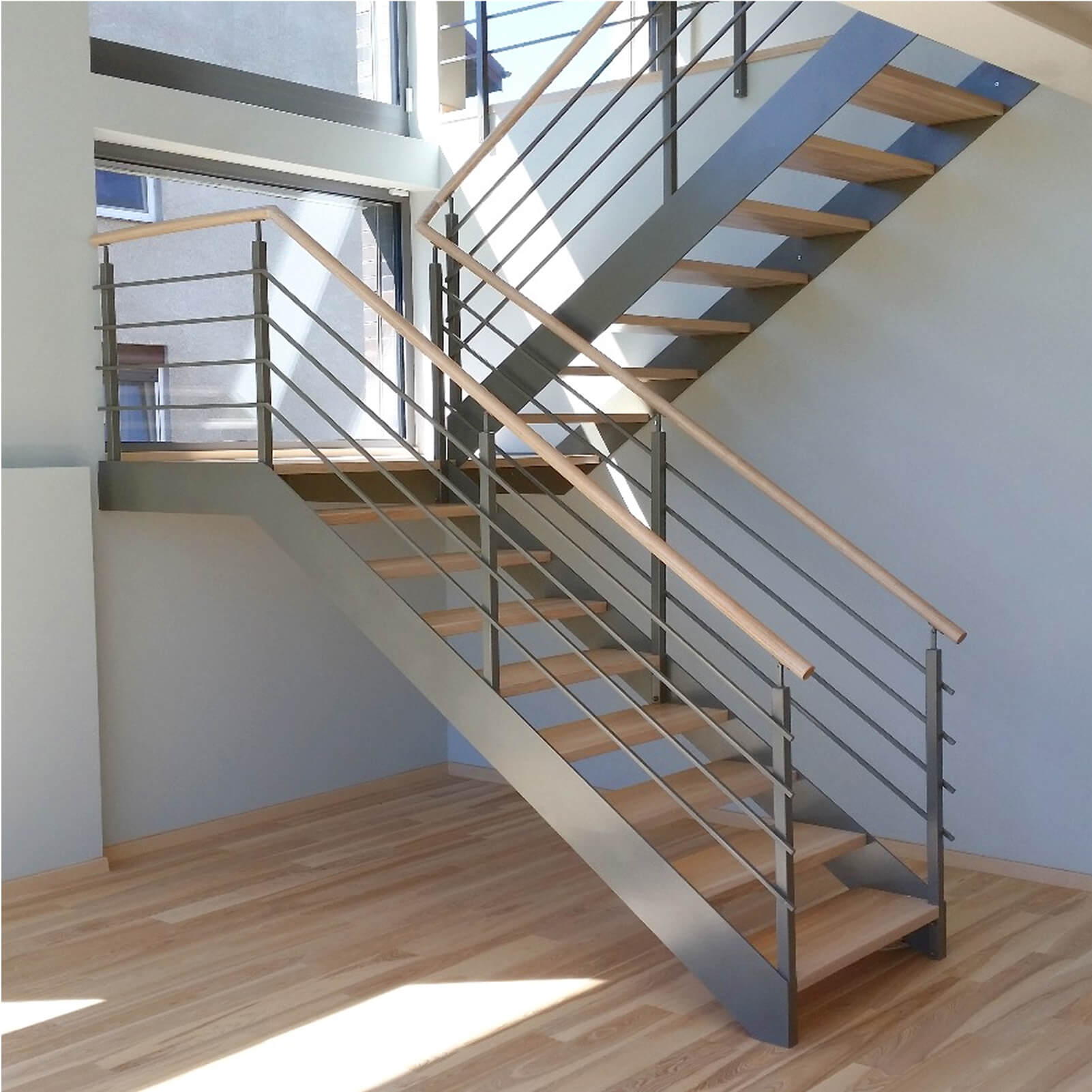 Minimalistyczne schody L-kształtne z malowanym stalowym stringerem i drewnianą poręczą