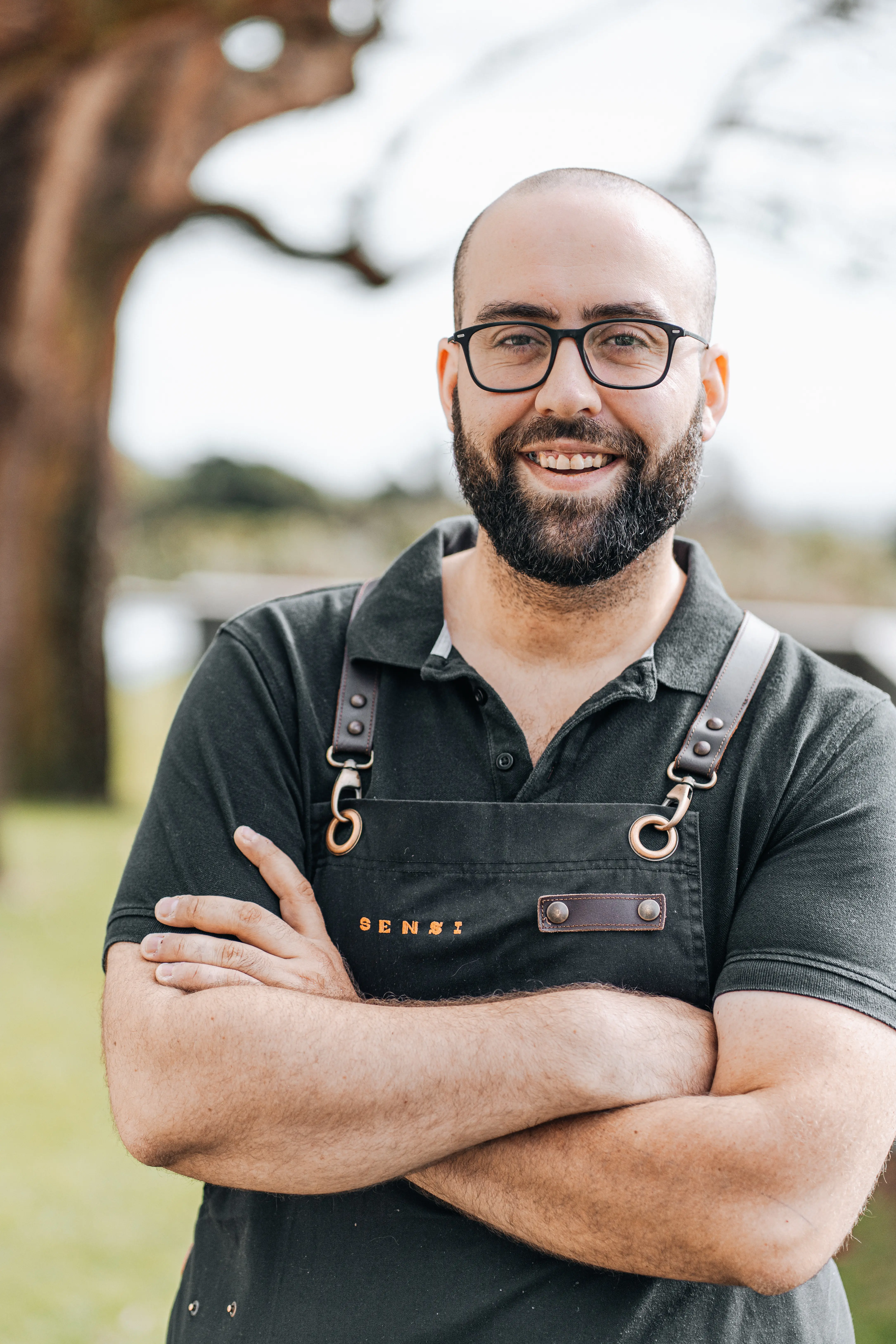 a man with a beard and glasses standing with his arms crossed