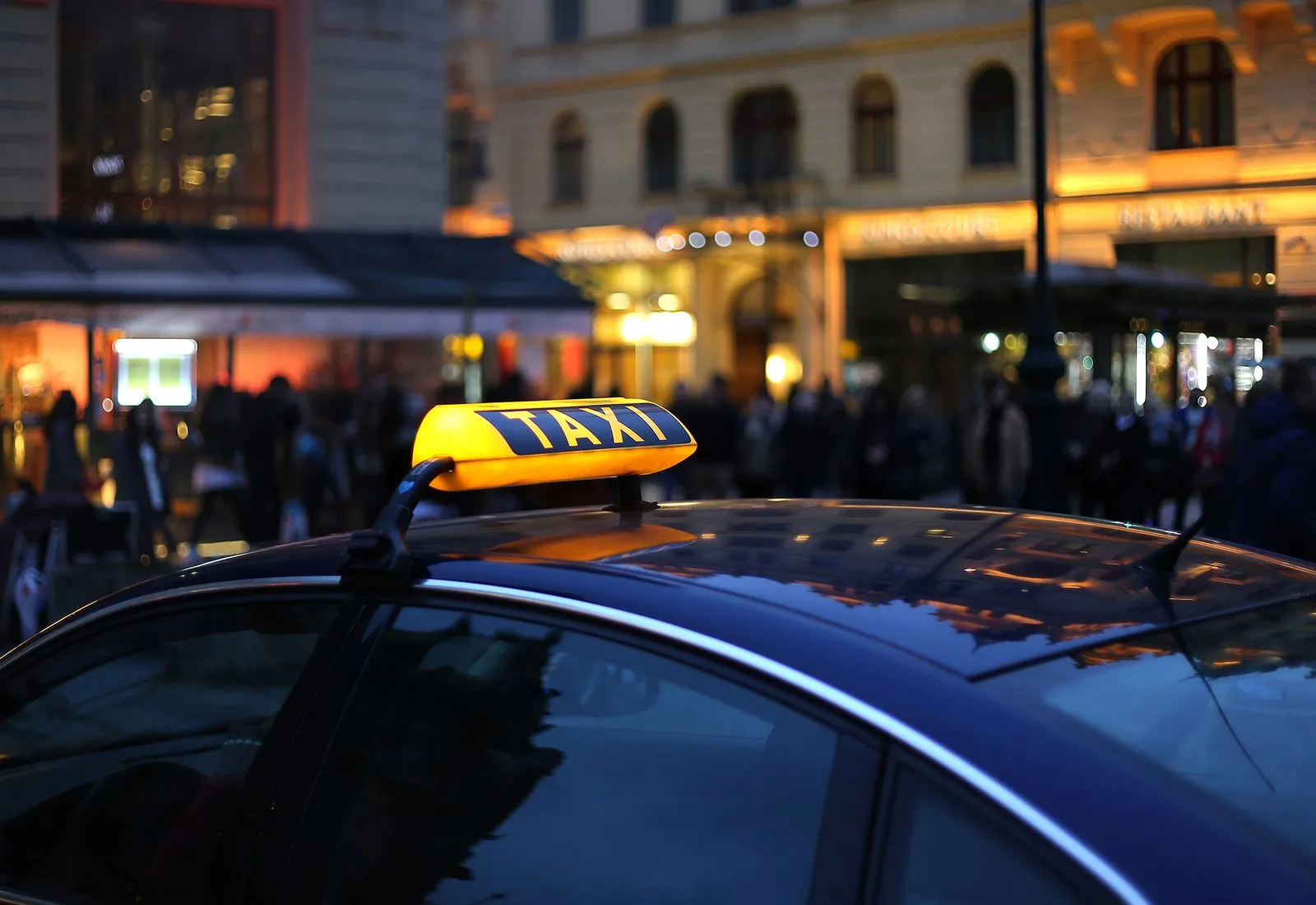 Toit d'une voiture avec un panneau lumineux jaune « TAXI » la nuit en ville animée.