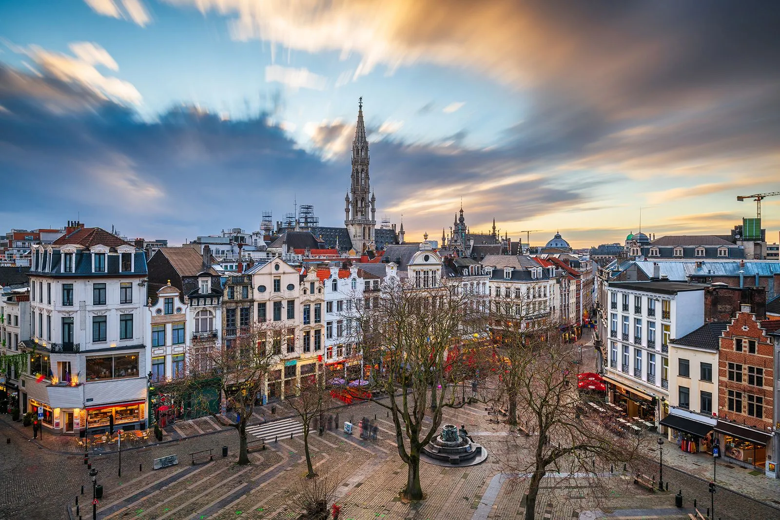 Vue panoramique de la Grand-Place de Bruxelles avec des bâtiments historiques et un ciel nuageux au coucher du soleil.