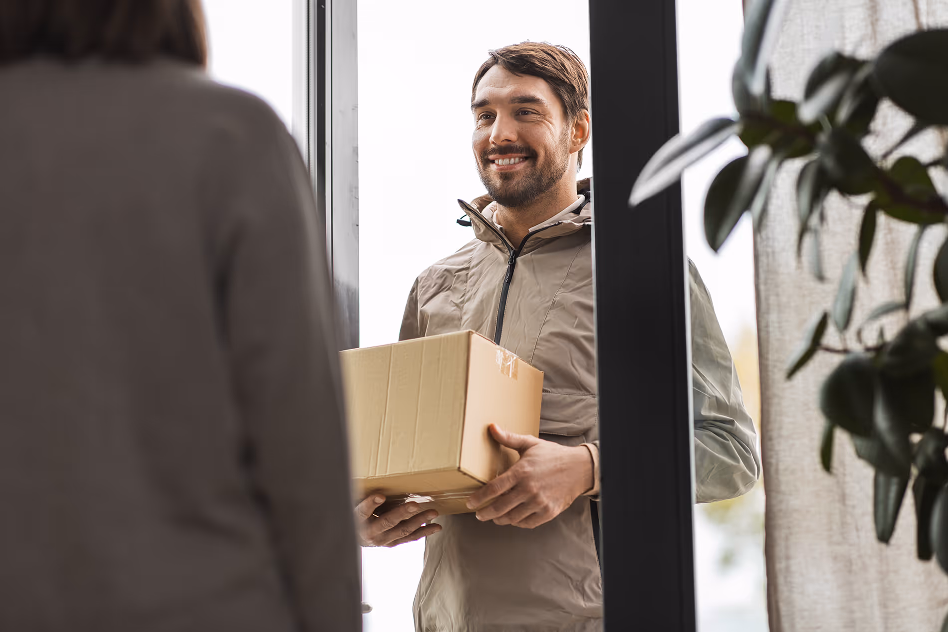 Livreur souriant tenant un colis en carton à la porte d'entrée d'une maison.