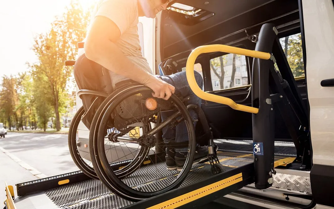 Un homme en fauteuil roulant monte dans un van accessible via une rampe.
