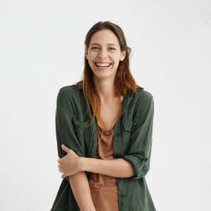 Woman with wide smile dressed in green jacket and brown t-shirt smiling broadly being happy to meet you