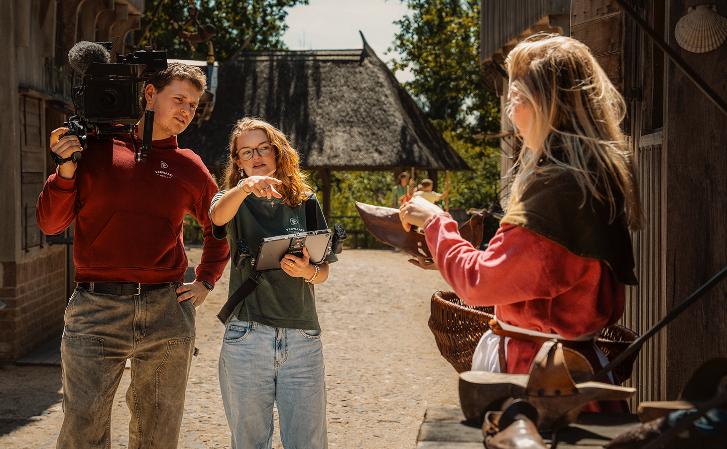 Cameraman en regisseur bespreken een scène met presentatrice Vera tijdens de opnames van de campagnefilm in Archeon.