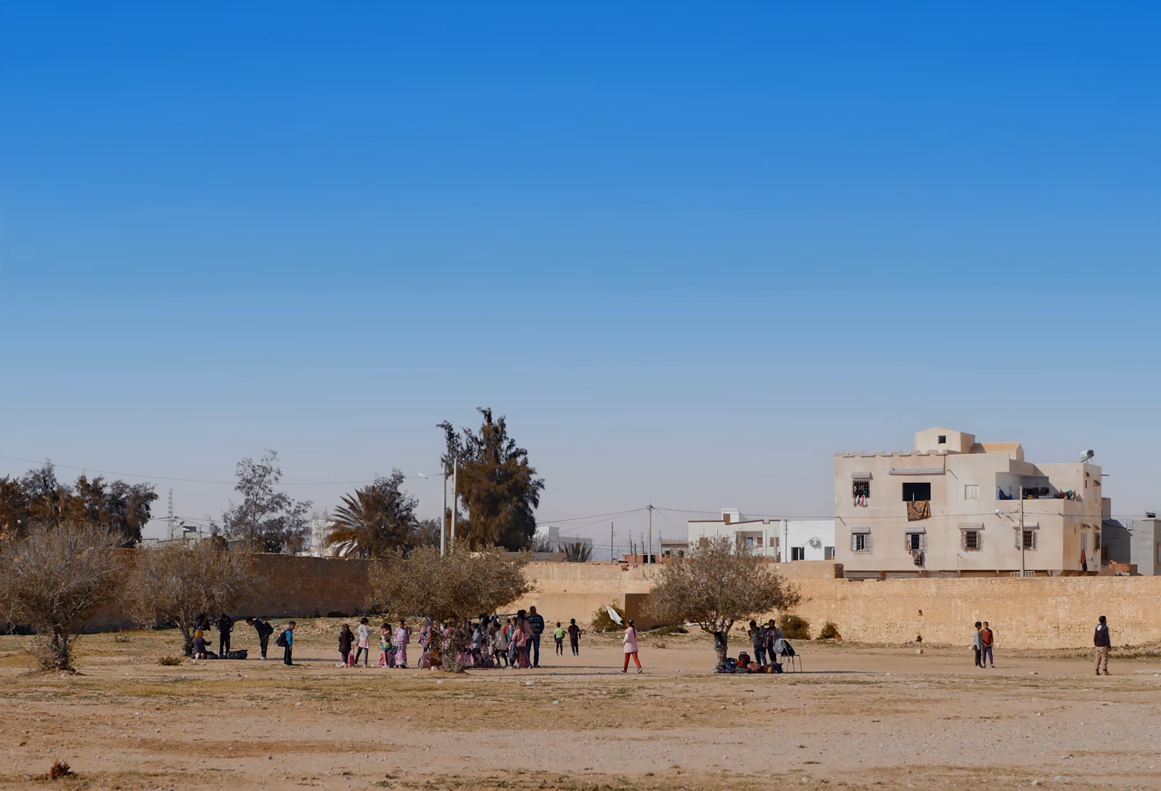 The landscape of a remote Tunisian village, with old buildings in the backdrop and children playing on a playground in the foreground.