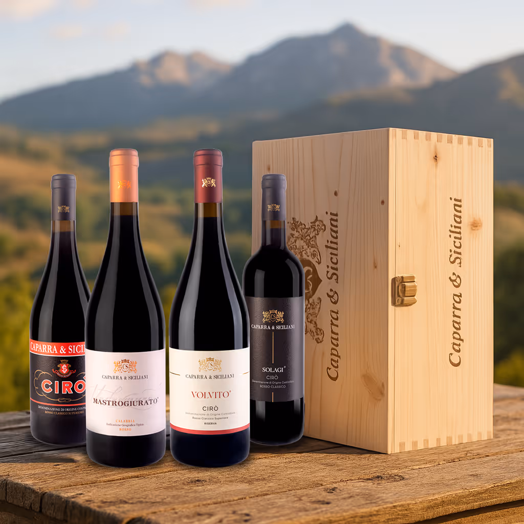 Vier Flaschen Wein von Caparra & Siciliani und eine hölzerne Weinkiste stehen auf einem Holztisch im Freien mit den Bergen im Hintergrund.