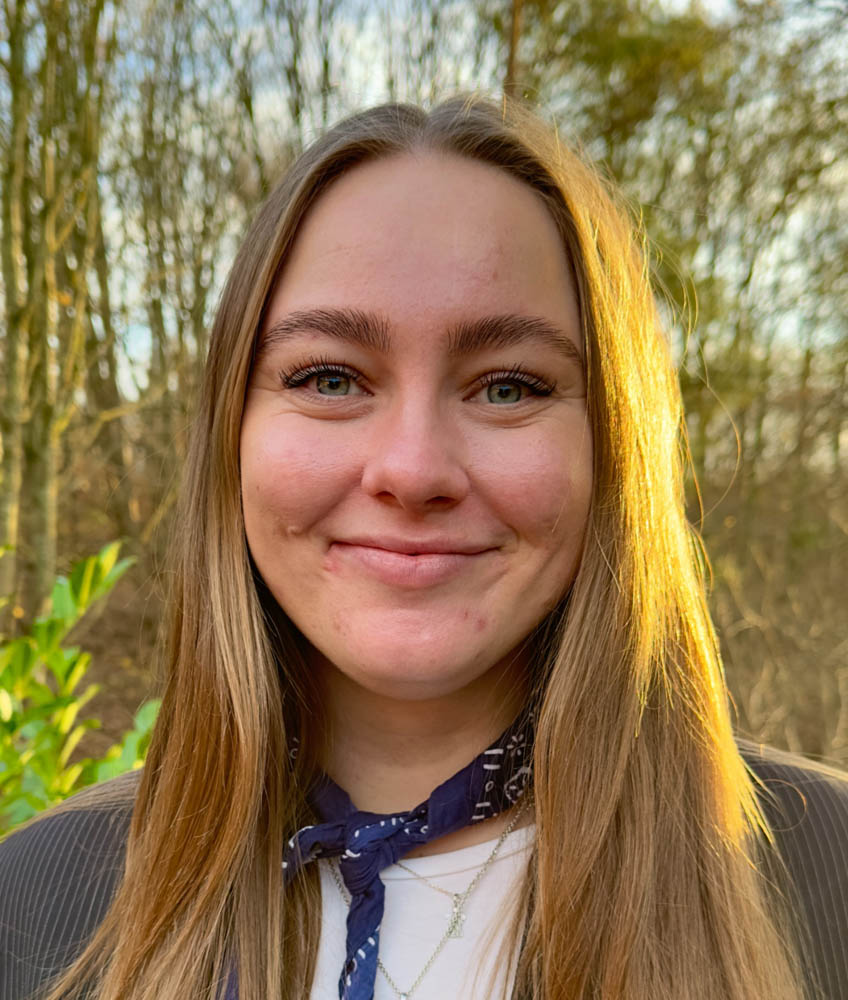 Frida - beboer på Jobkollegiet med langt blondt hår og blåt tørklæde, smiler foran kameraet i naturlige omgivelser