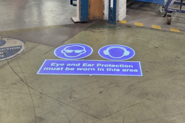 Projected floor signage indicating PPE zone in aerospace facility