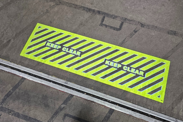 Yellow hatched projected floor sign with 'Keep Clear' text in aerospace engine facility