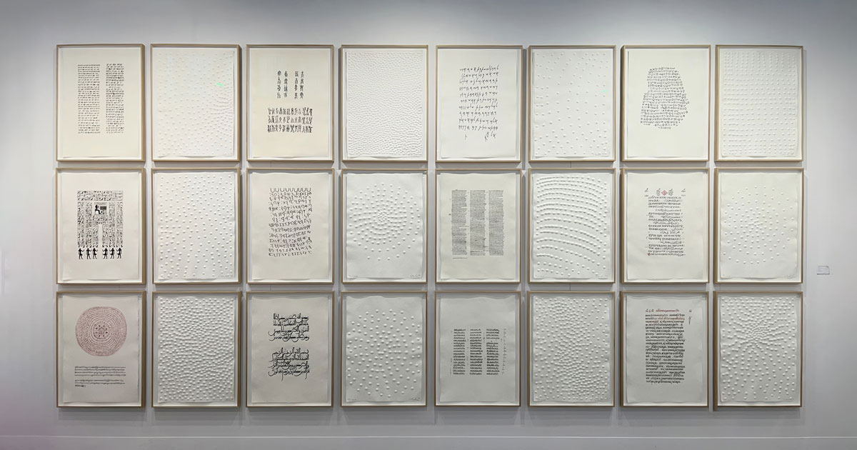 Galeriewand von Günther Uecker mit 24 gerahmten Kunstwerken, die abwechselnd Blindrägungen und handgeschriebene Schriftzeichen oder kalligrafische Texte zeigen.