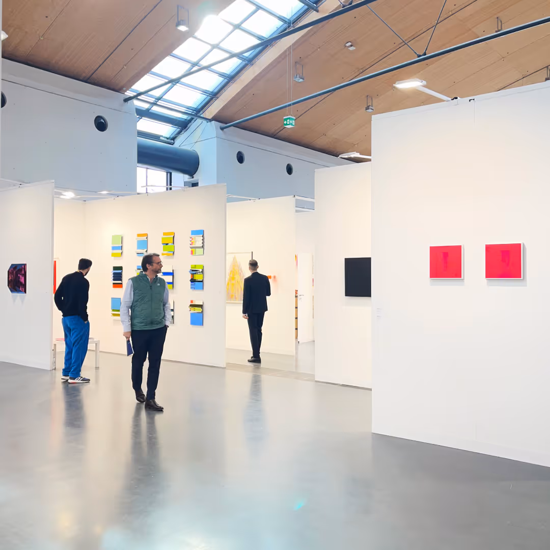 Besucher in einer modernen Kunstgalerie betrachten bunte und abstrakte Gemälde an weißen Wänden unter einem hohen Glasdach.