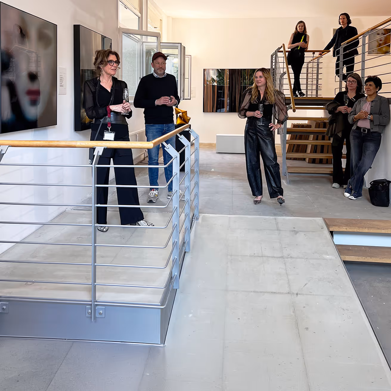 Sechs Personen halten ein Glas und unterhalten sich in einer modernen Galerie mit Kunstwerken an den Wänden.