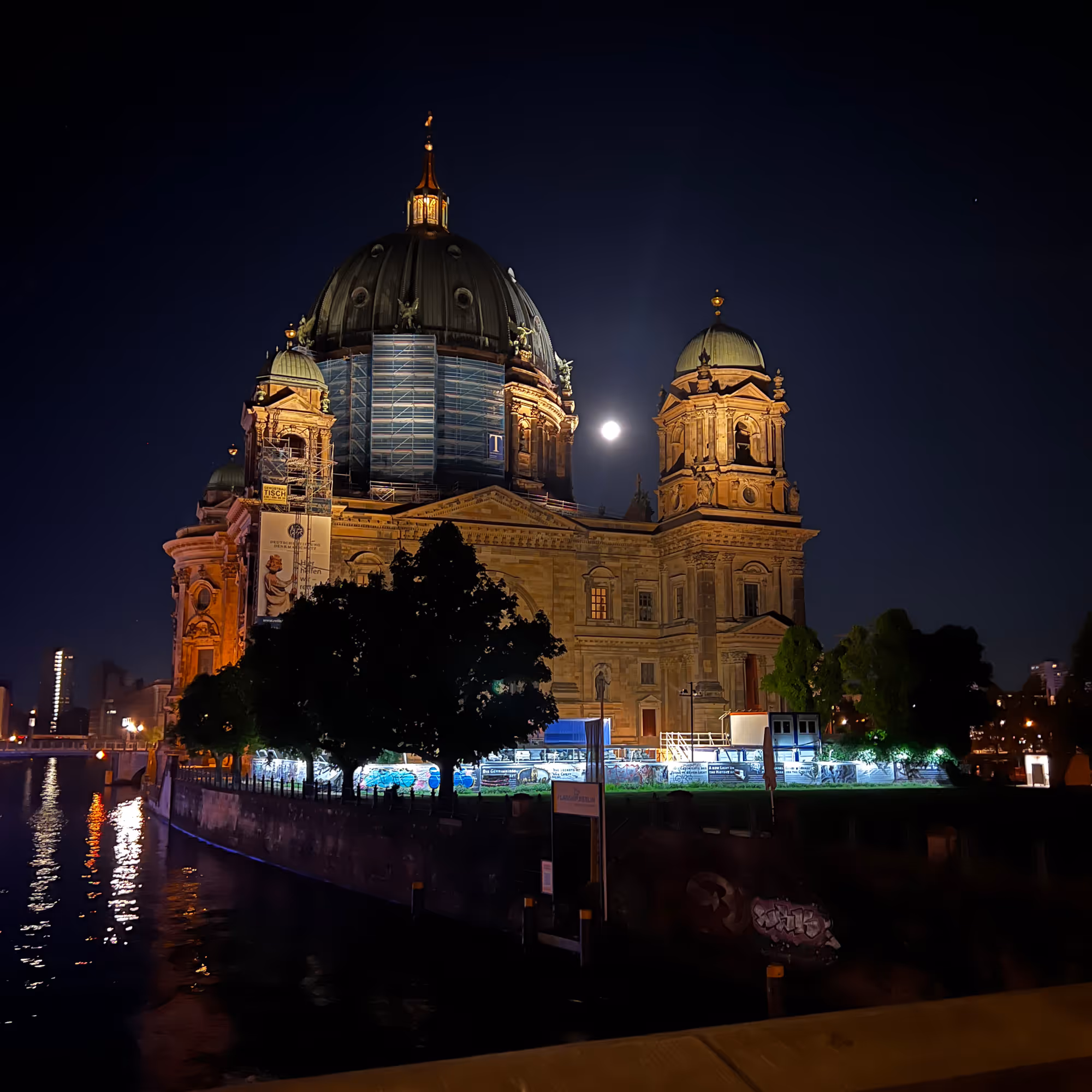 Nächtliche Ansicht des Berliner Doms mit beleuchteter Fassade und hellem Vollmond im Hintergrund.