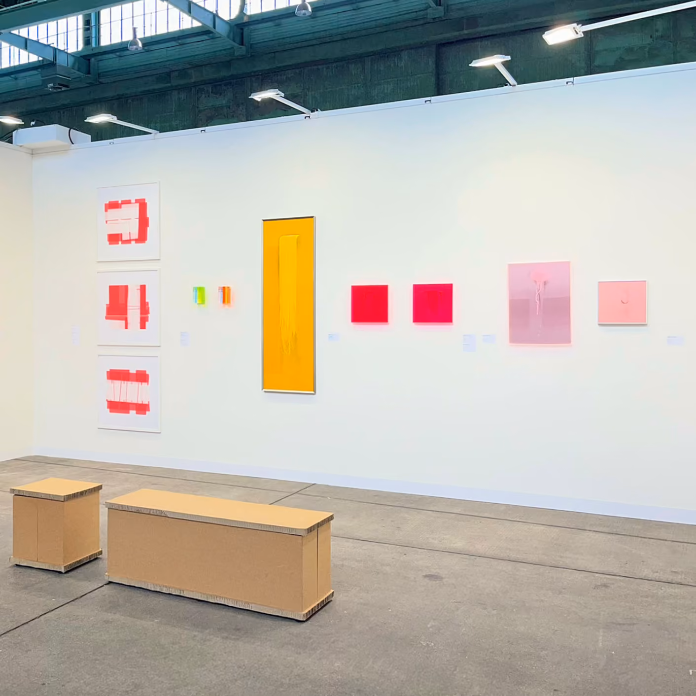 Moderner Ausstellungsraum mit weißen Wänden, farbigen abstrakten Gemälden und einer Person mit Broschüre.