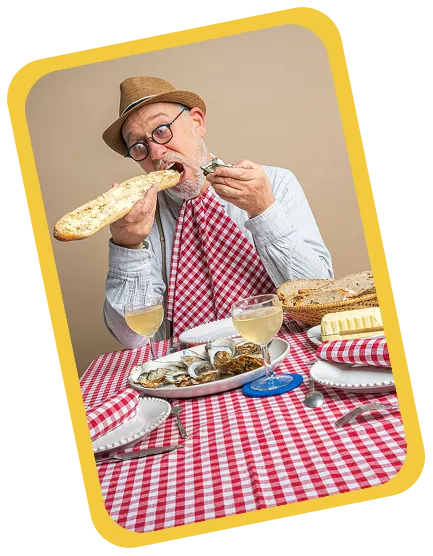 Un homme âgé avec chapeau et lunettes mange une huître avec une grande baguette, assis à une table à nappes rouges à carreaux avec des verres de vin blanc et un plateau d'huîtres.