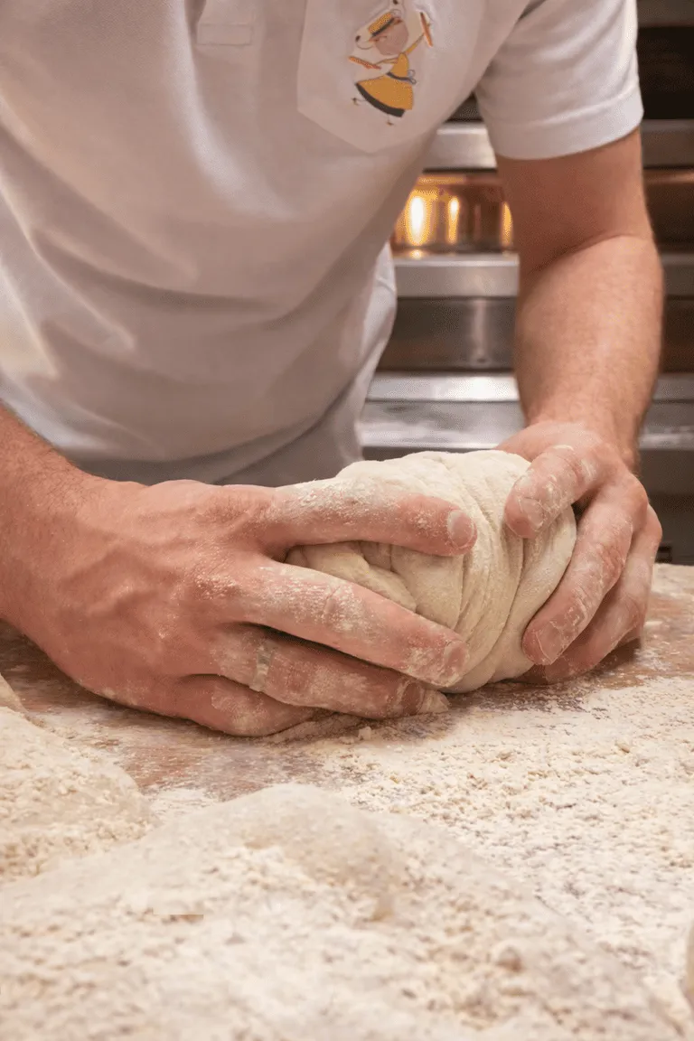 Personne pétrissant une boule de pâte sur une surface recouverte de farine.