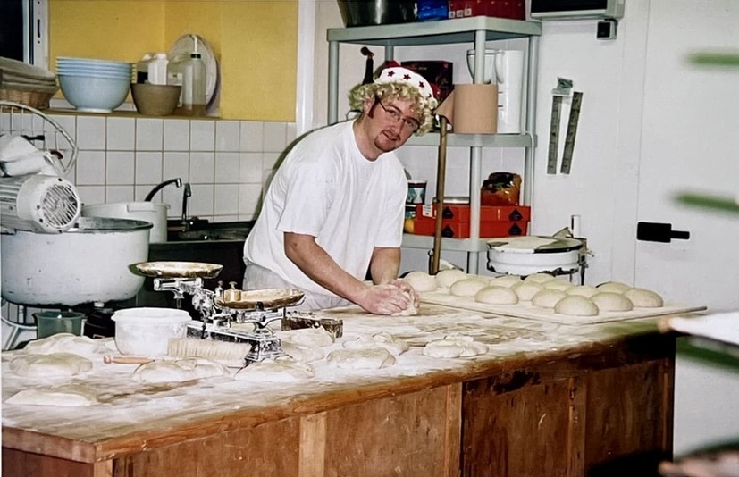 Boulanger avec un bonnet étoilé travaillant la pâte sur une table en bois dans une boulangerie.