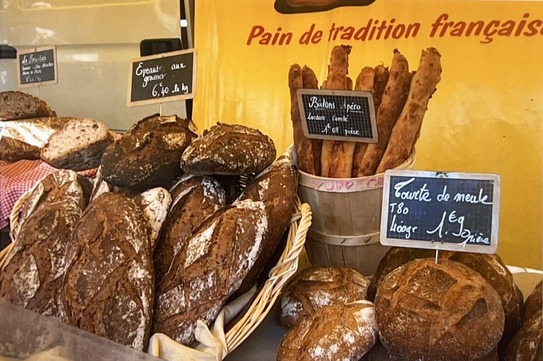 Différents pains artisanaux français disposés sur un étal avec des étiquettes de prix et un panneau jaune indiquant Pain de tradition française.