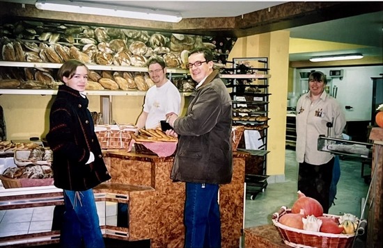 Quatre personnes dans une boulangerie entourées de pains et de citrouilles, souriantes et en interaction.