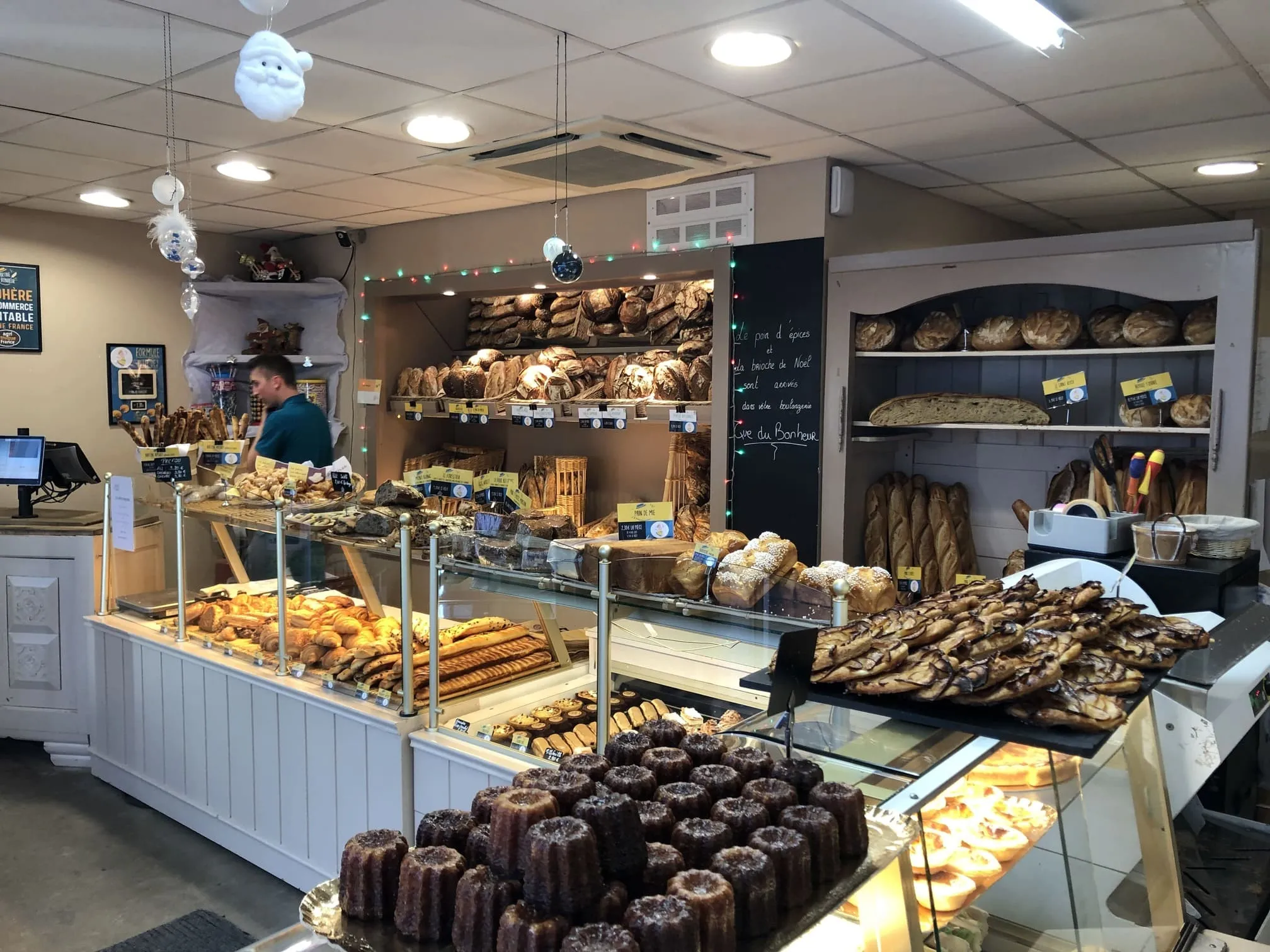 Intérieur d'une boulangerie avec un comptoir vitré rempli de pâtisseries, divers pains sur les étagères et un employé en arrière-plan.