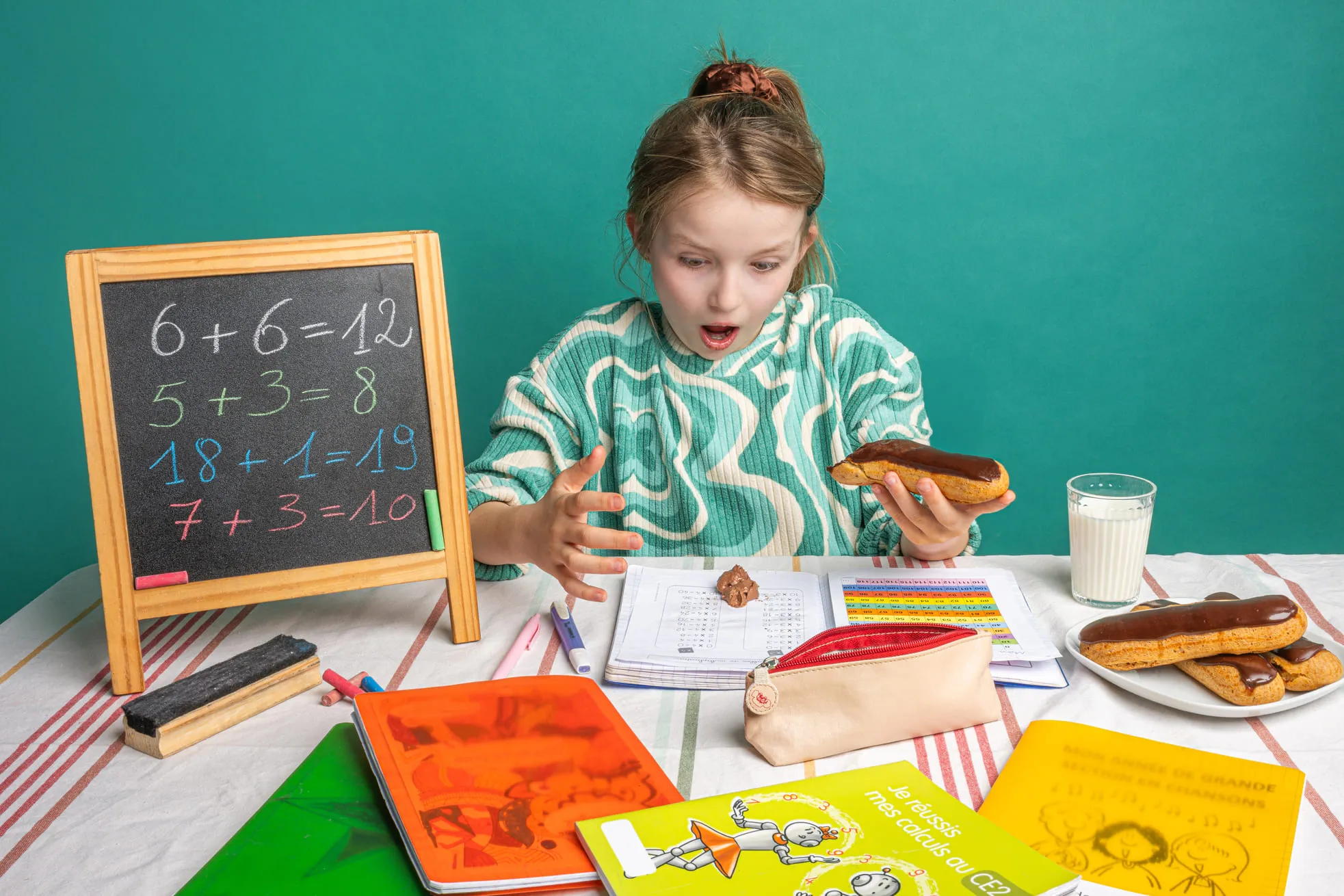 Fille surprise par un dessin de chocolat sur ses devoirs de mathématiques avec un éclair au chocolat en main.