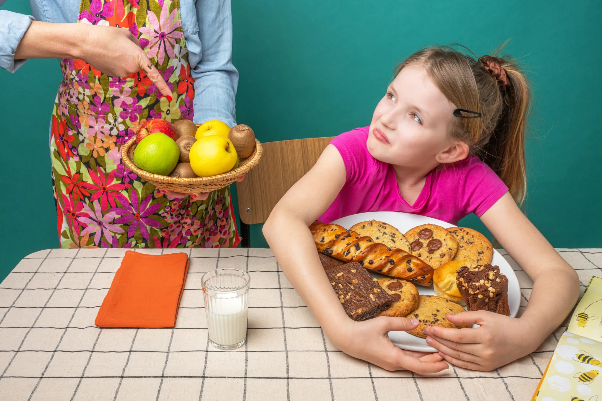 Une fille en rose regarde avec hésitation un panier de fruits pendant qu’on lui présente des pâtisseries.