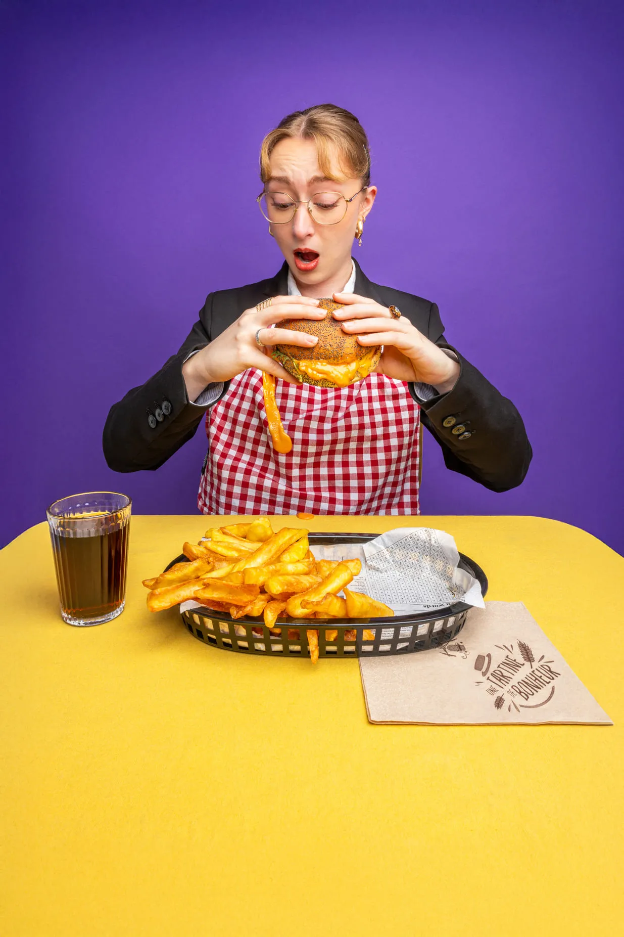 Personne surprise devant un hamburger au fromage coulant, avec des frites et une boisson à table.