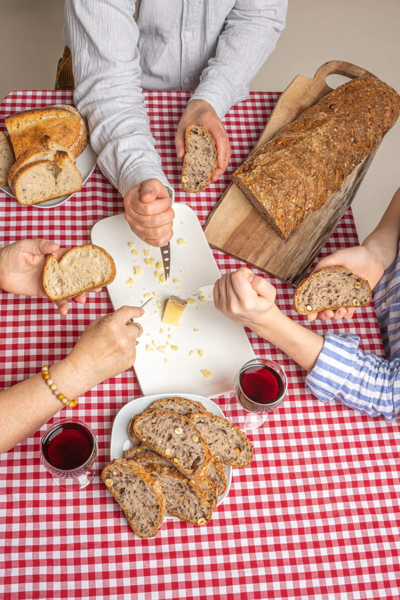 Trois personnes tiennent des tranches de pain avec du fromage sur une table à nappe vichy rouge.
