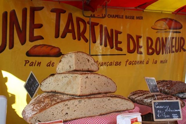 Grande pile de pain artisanal français devant une bannière jaune avec texte promotionnel.