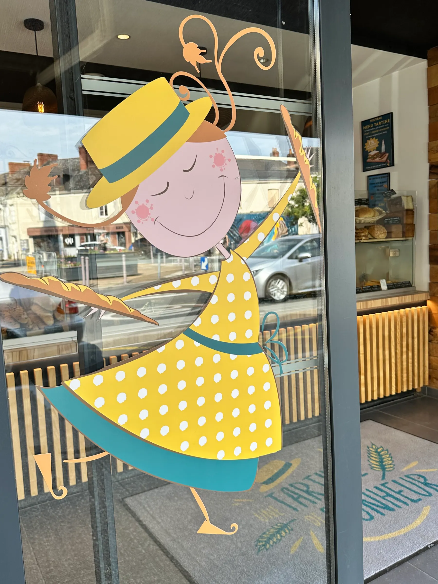Dessin d'une fille souriante en robe jaune à pois tenant deux baguettes sur une vitre de magasin.