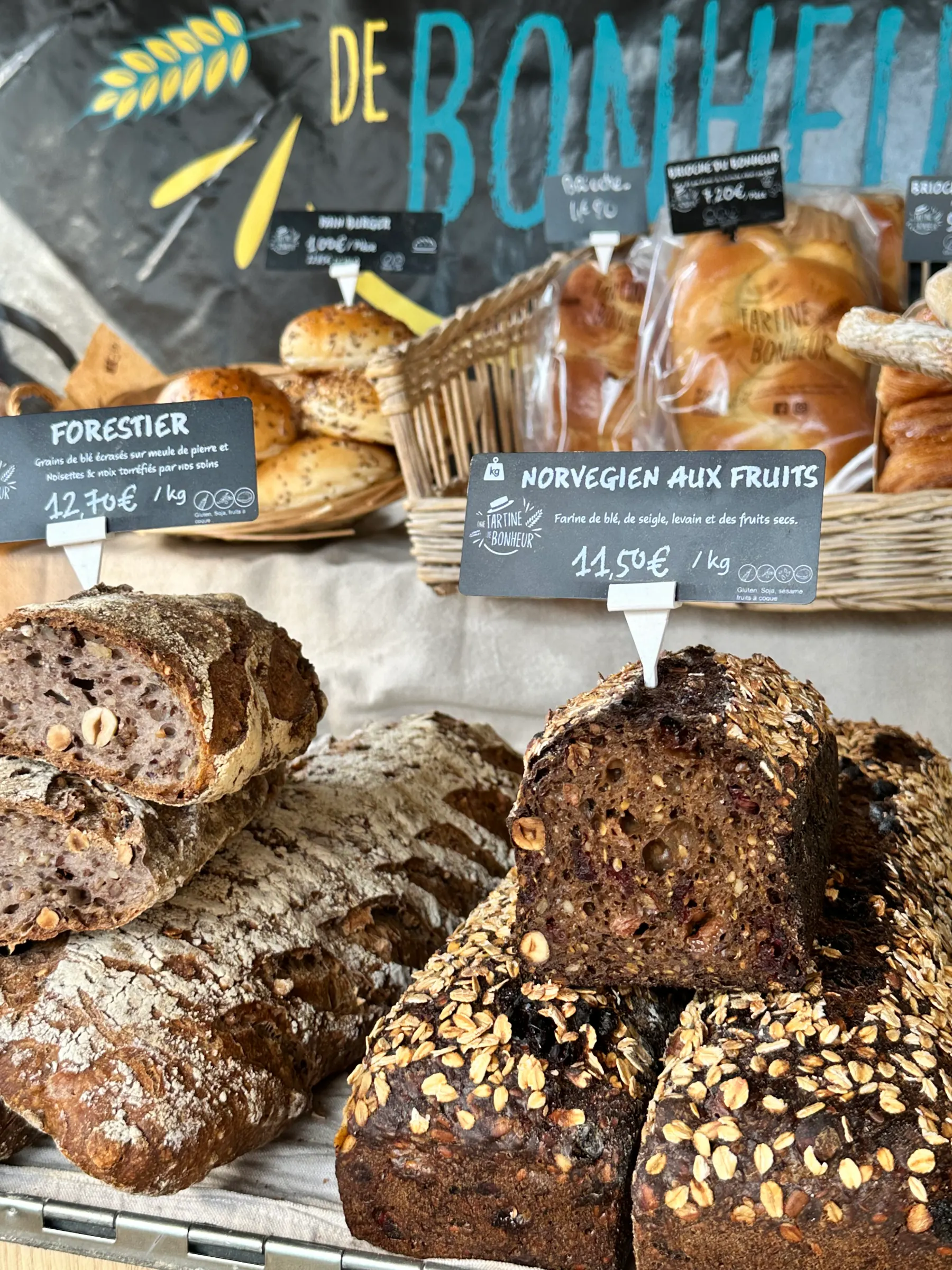 Pains variés avec étiquettes, dont pain forestier aux noisettes et pain norvégien aux fruits.