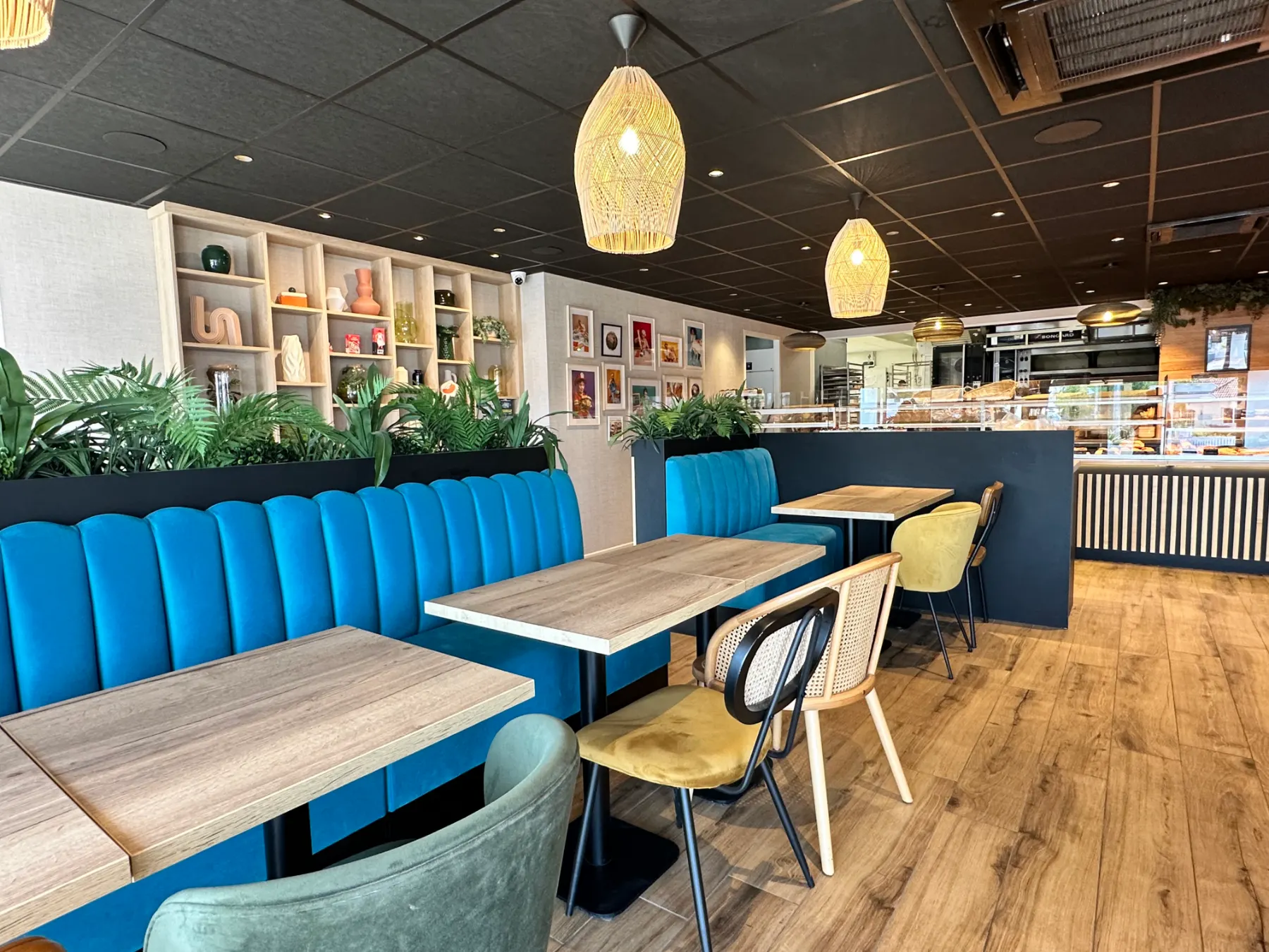 Intérieur d'un café moderne avec banquettes bleues, chaises variées et éclairage suspendu en rotin.