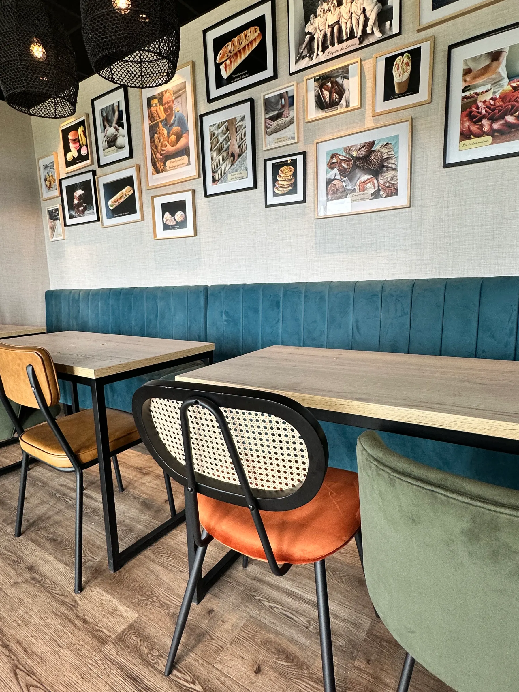 Intérieur d'un café avec tables en bois, chaises colorées et photos encadrées sur le mur.