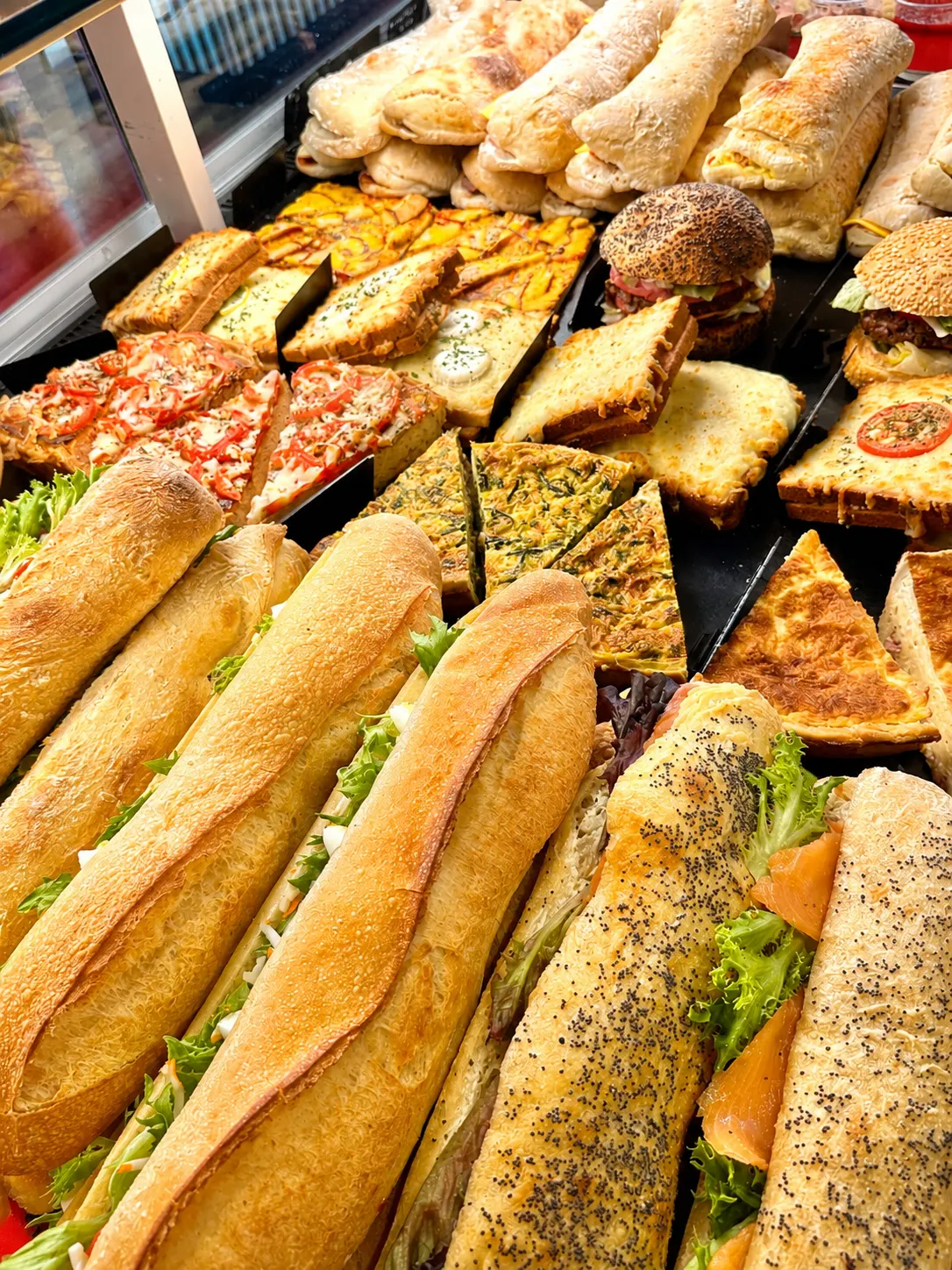 Vitrine avec sandwichs, pizzas, quiches, burgers et toasts variés.
