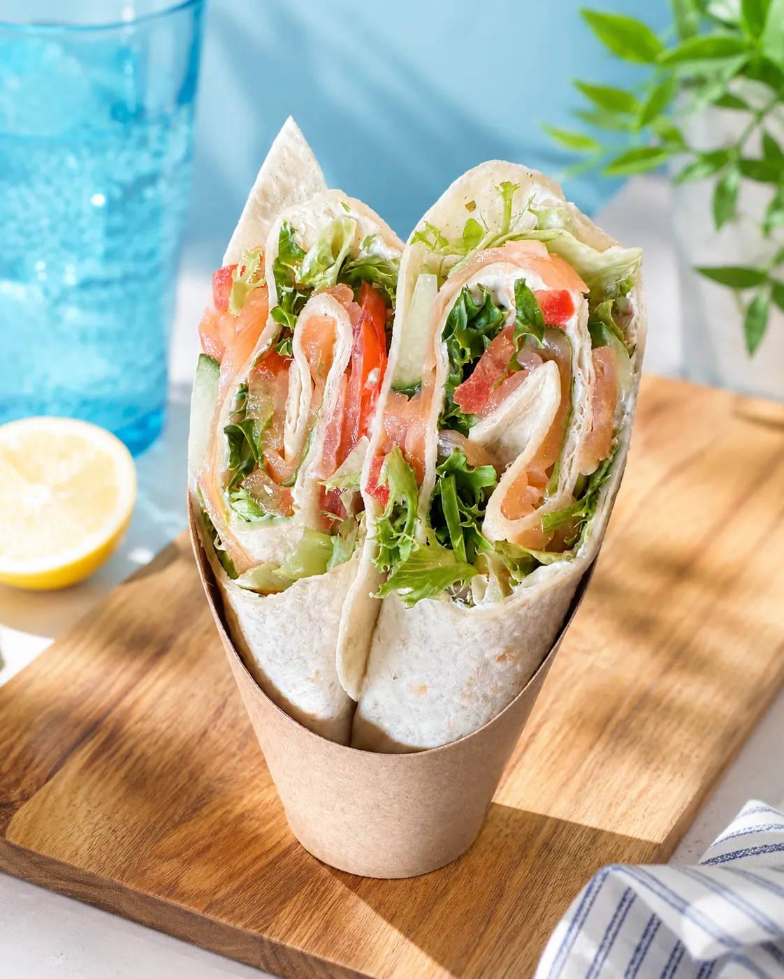 Deux wraps garnis de saumon fumé, laitue et sauce dans un emballage en papier sur une planche en bois.