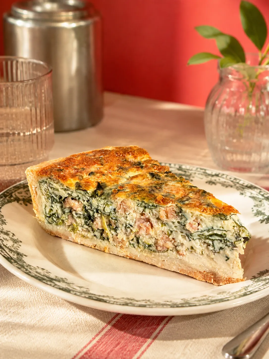 Une part de quiche aux légumes verts et au jambon sur une assiette décorative.