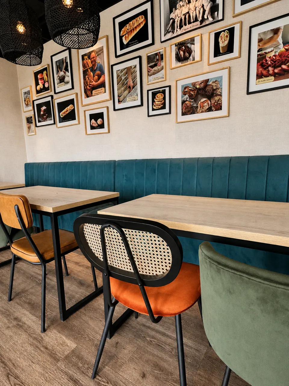 Coin repas avec tables en bois, chaises colorées, banquette bleue et photos de pâtisseries au mur.