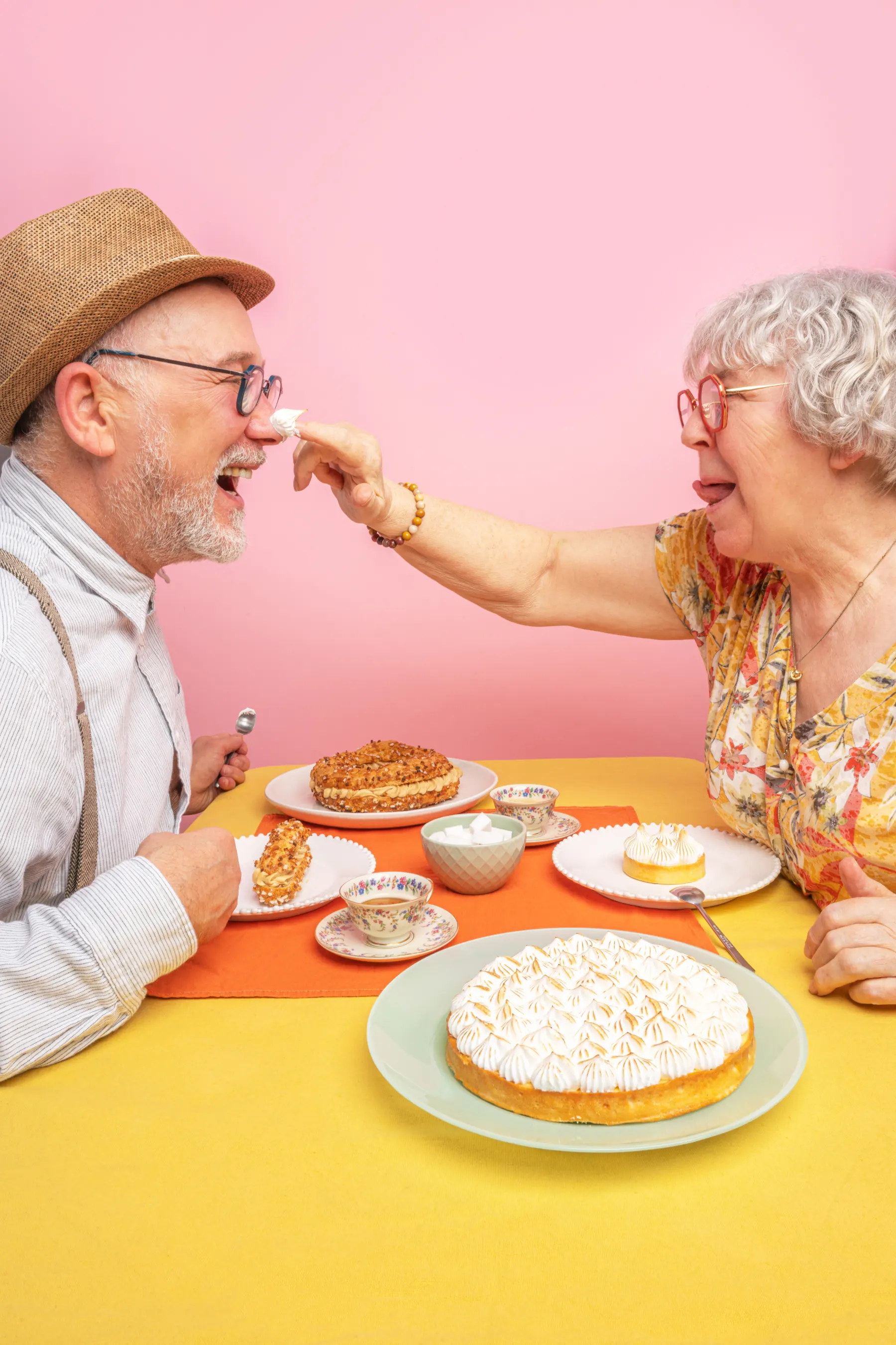 Un couple âgé souriant joue en mettant de la crème sur le nez de l'homme à table.