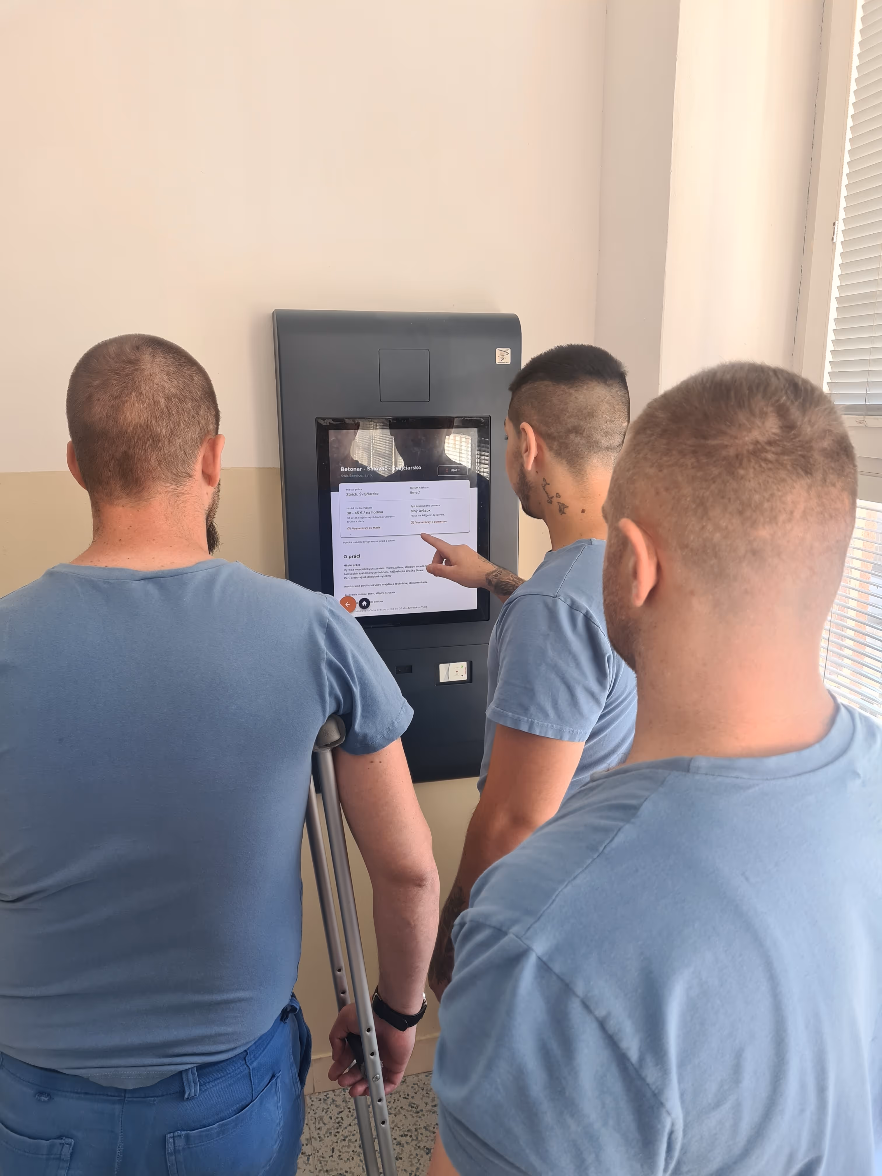 Skupina odsúdených osôba používajúca nástenný kiosk s aplikáciou Holup