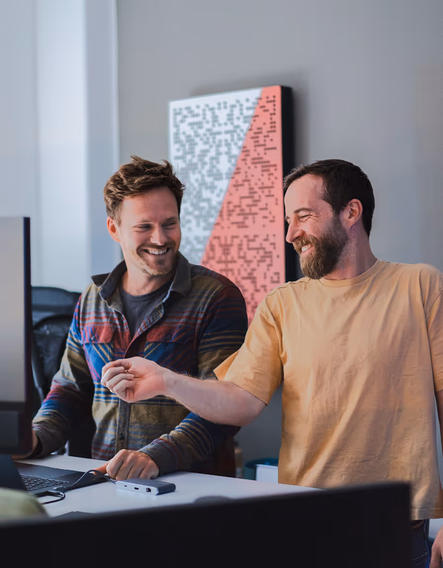 Zwei Männer in einem Büro diskutieren ein Webflow Projekt, während sie auf einen Bildschirm deuten.