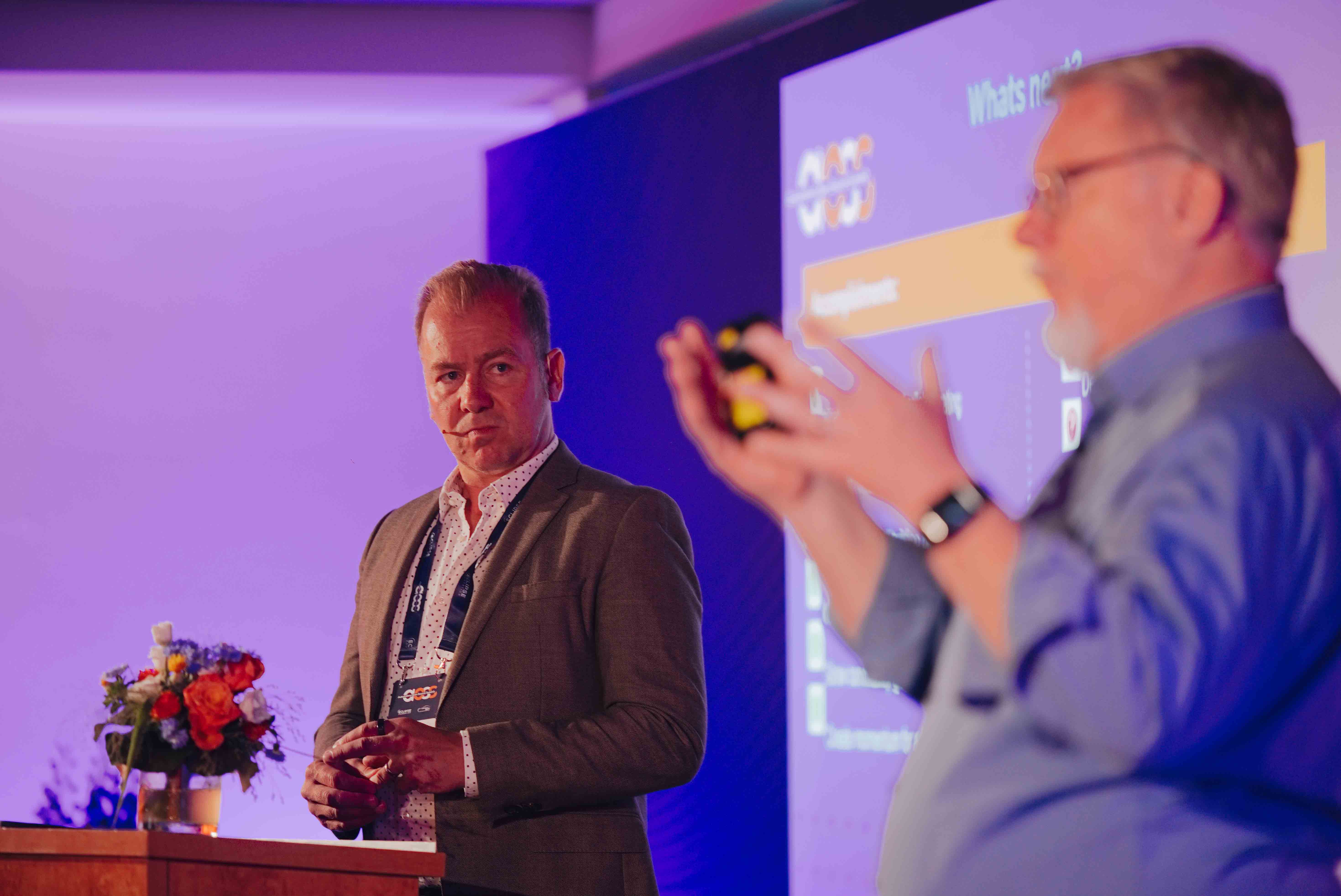 Twee sprekers op het podium met projectieschermen tijdens de Automotive Open Source Summit in Starnberg