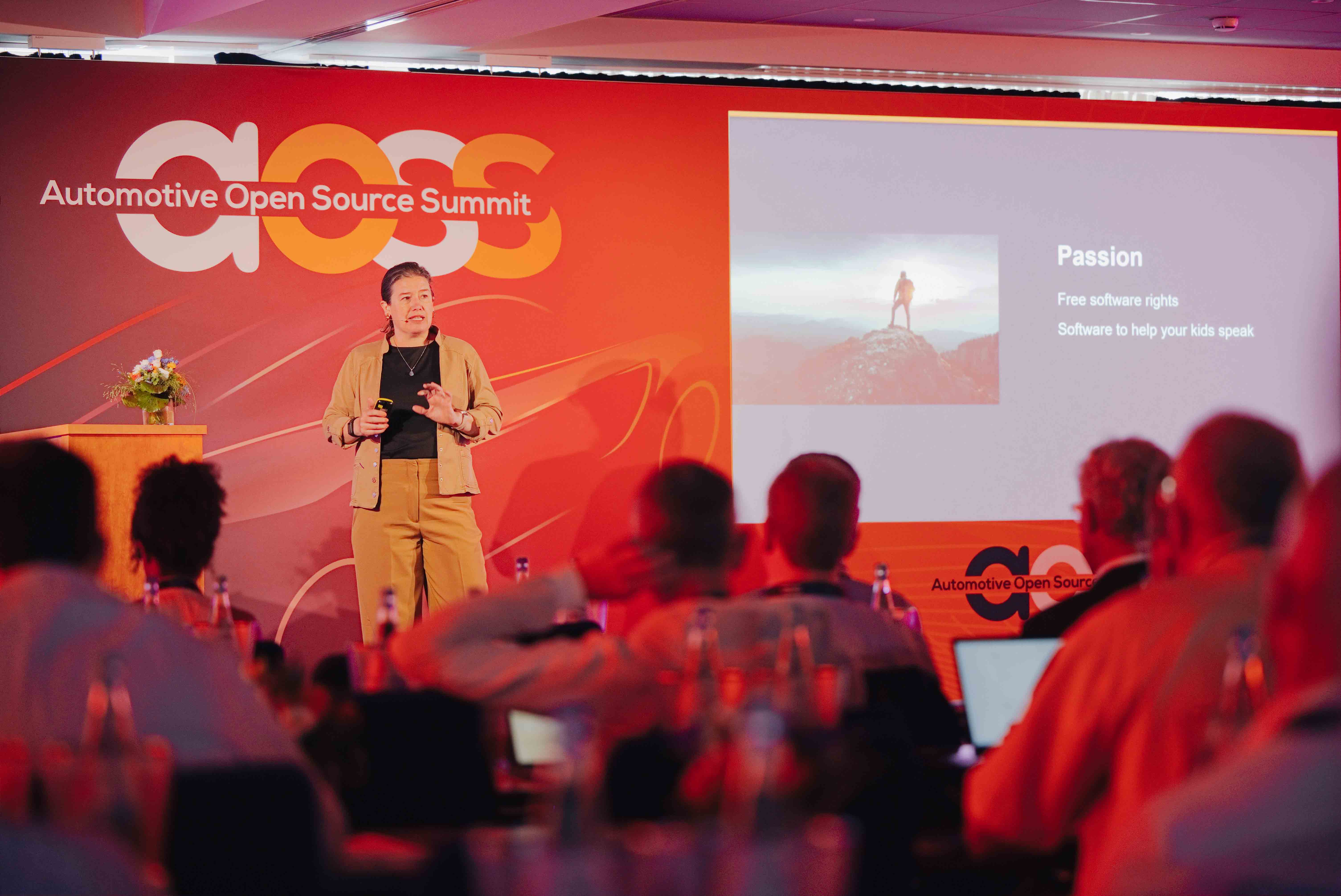 Spreker op het podium van de Automotive Open Source Summit in Starnberg met projectiescherm op de achterwand